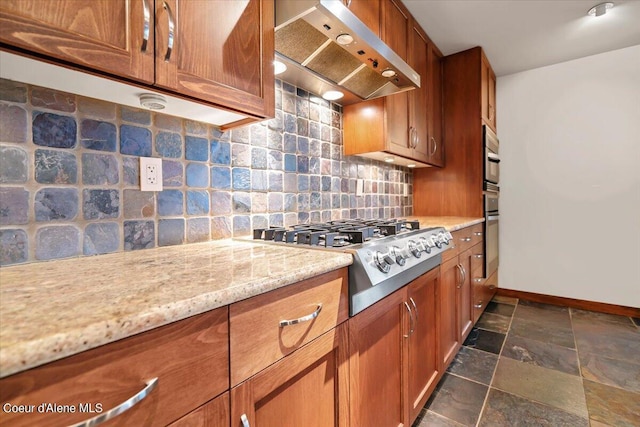 kitchen with light stone counters, decorative backsplash, appliances with stainless steel finishes, stone finish floor, and exhaust hood