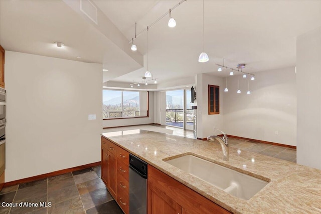 kitchen with decorative light fixtures, a sink, light stone countertops, brown cabinetry, and glass insert cabinets