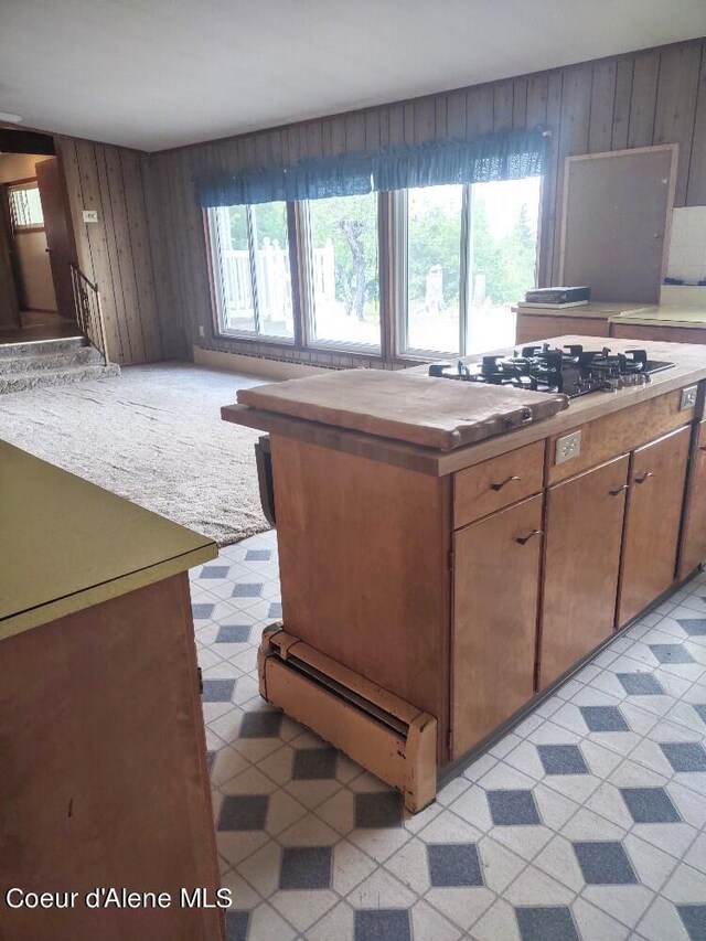 kitchen featuring stainless steel gas cooktop, light carpet, and wood walls