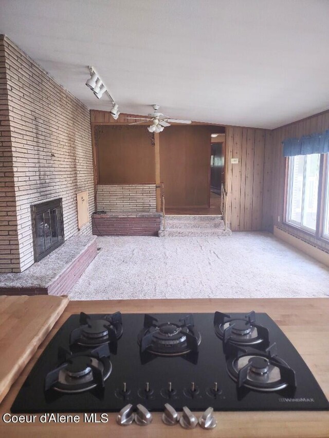 kitchen with ceiling fan, a fireplace, track lighting, black gas stovetop, and wood walls