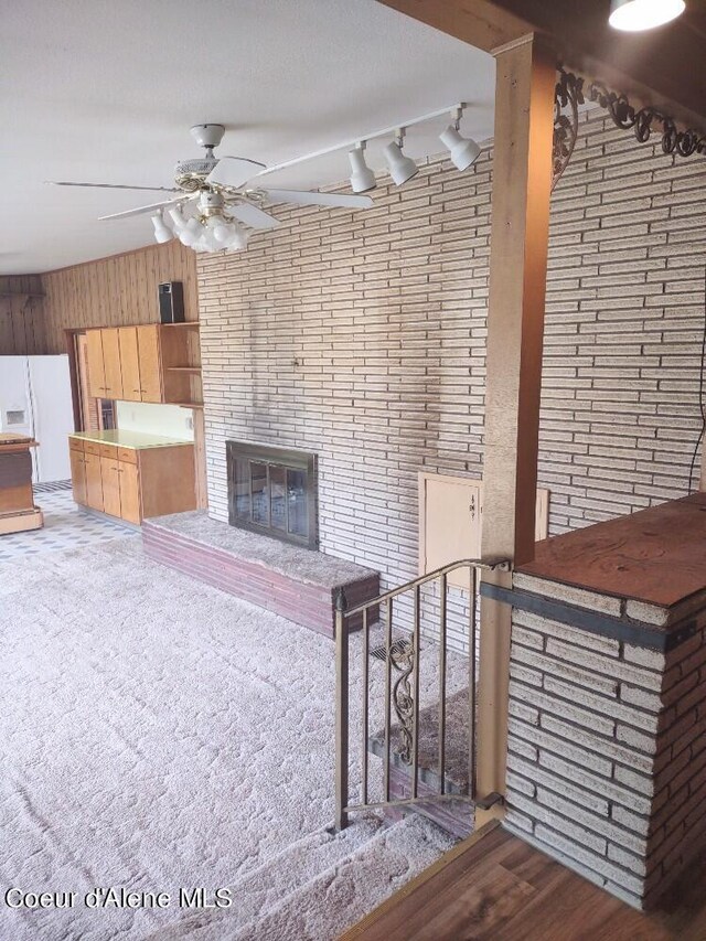 unfurnished living room with hardwood / wood-style flooring, rail lighting, ceiling fan, wooden walls, and a brick fireplace