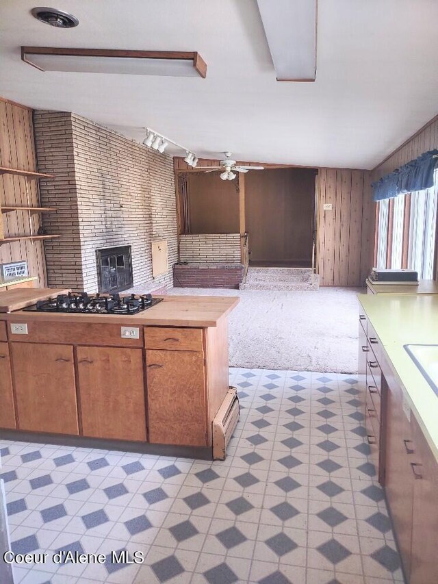 kitchen featuring wooden walls, ceiling fan, baseboard heating, black gas stovetop, and light carpet