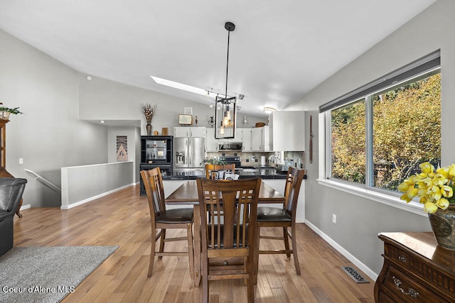 dining space with vaulted ceiling with skylight, sink, and light hardwood / wood-style flooring