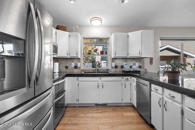 kitchen with sink, tasteful backsplash, white cabinetry, stainless steel appliances, and light wood-type flooring