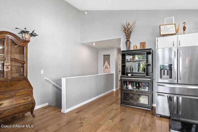 kitchen featuring white cabinets, light wood-type flooring, stainless steel fridge, and high vaulted ceiling