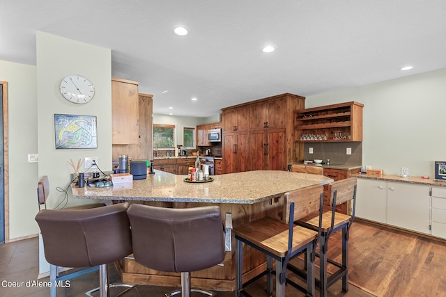 kitchen featuring kitchen peninsula, backsplash, light stone countertops, a kitchen breakfast bar, and dark hardwood / wood-style flooring