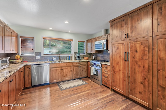 kitchen with appliances with stainless steel finishes, sink, light stone counters, decorative backsplash, and wood-type flooring