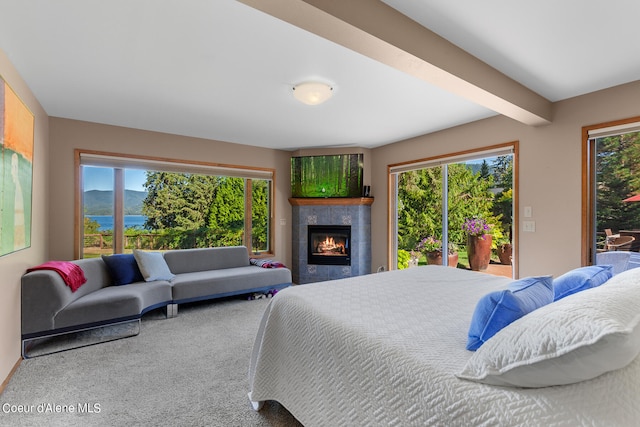 carpeted bedroom with beamed ceiling, a tiled fireplace, and access to outside