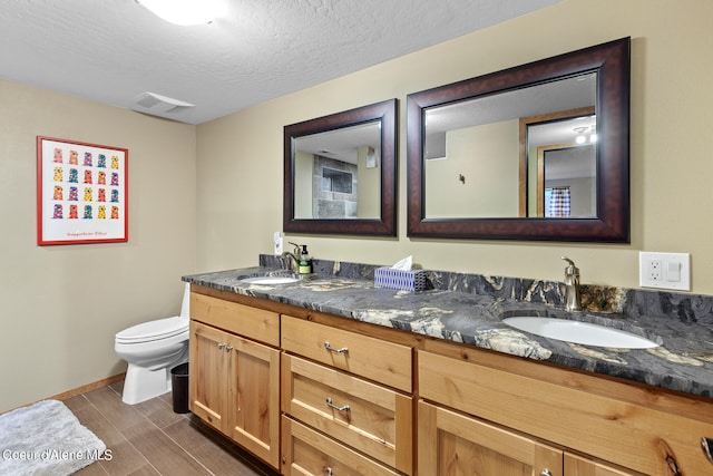 bathroom featuring a textured ceiling, toilet, and dual bowl vanity