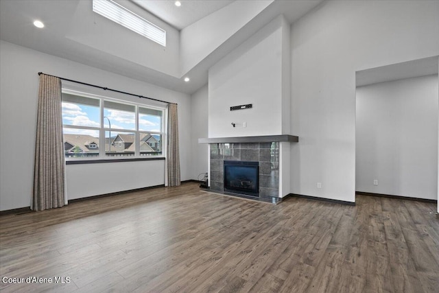 unfurnished living room with a tiled fireplace, wood-type flooring, and a high ceiling