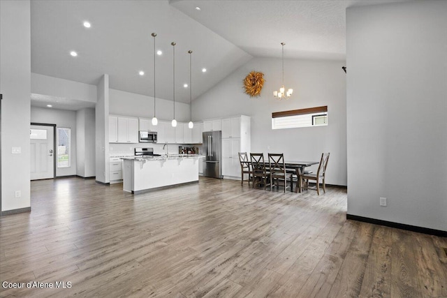 kitchen with wood-type flooring, appliances with stainless steel finishes, pendant lighting, a kitchen island with sink, and white cabinets