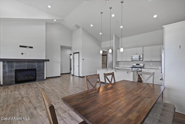 dining area featuring high vaulted ceiling, hardwood / wood-style flooring, and a tile fireplace