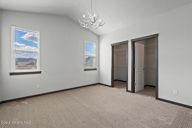 unfurnished bedroom with an inviting chandelier, vaulted ceiling, a textured ceiling, and carpet