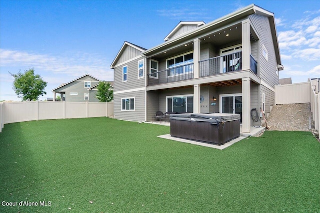 back of property featuring a hot tub, a balcony, a lawn, and a patio area