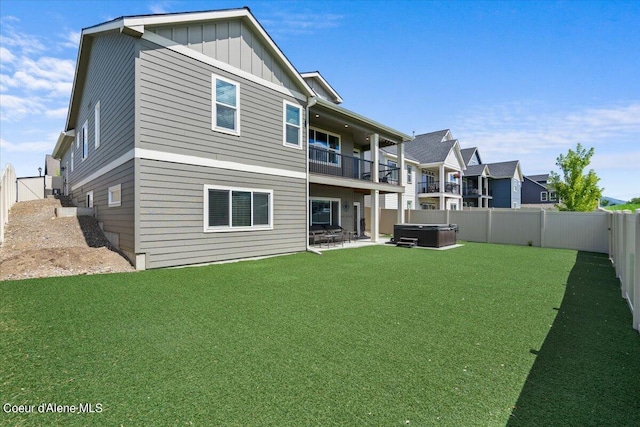 rear view of house featuring a hot tub, a balcony, and a yard