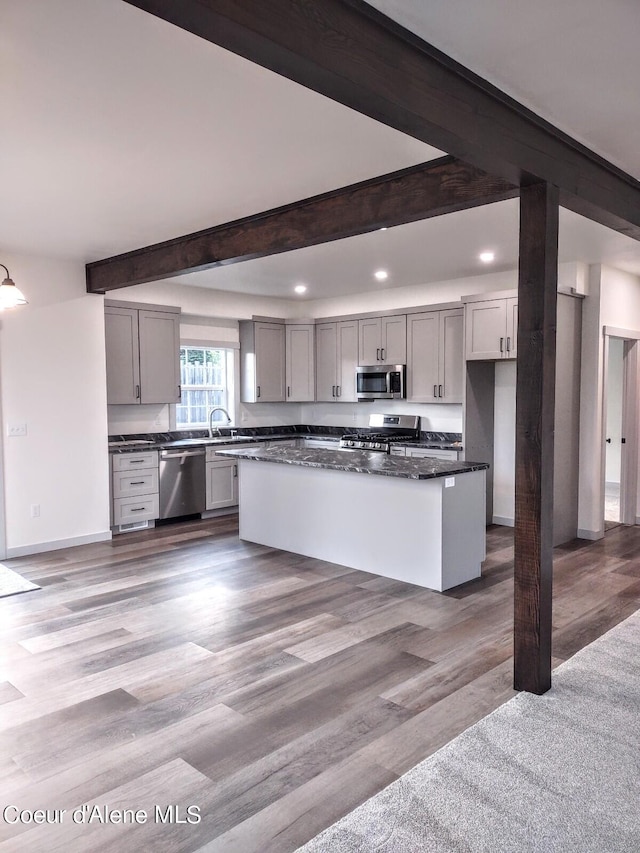 kitchen featuring gray cabinets, hardwood / wood-style flooring, beamed ceiling, a kitchen island, and appliances with stainless steel finishes