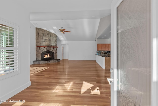 unfurnished living room featuring ceiling fan, a fireplace, vaulted ceiling, and light wood-type flooring