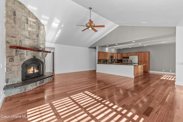 unfurnished living room featuring high vaulted ceiling, a fireplace, sink, ceiling fan, and light wood-type flooring