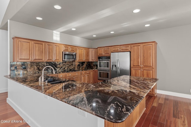 kitchen featuring sink, backsplash, stainless steel appliances, kitchen peninsula, and dark stone counters