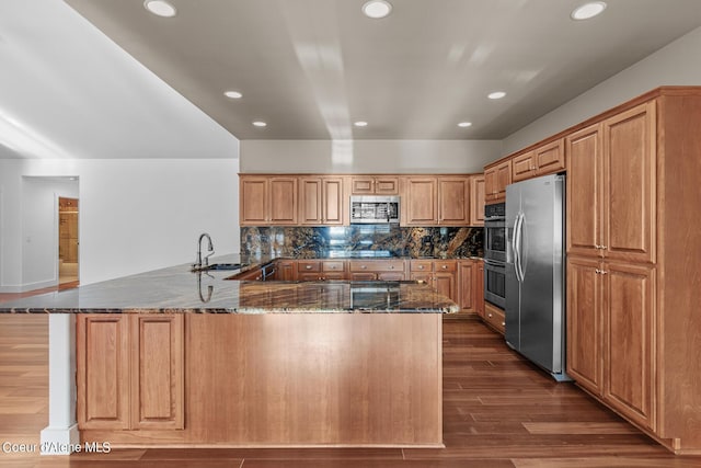 kitchen featuring sink, dark stone countertops, stainless steel appliances, dark hardwood / wood-style flooring, and kitchen peninsula