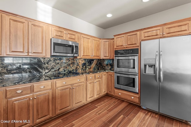 kitchen with appliances with stainless steel finishes, dark hardwood / wood-style floors, dark stone countertops, and decorative backsplash