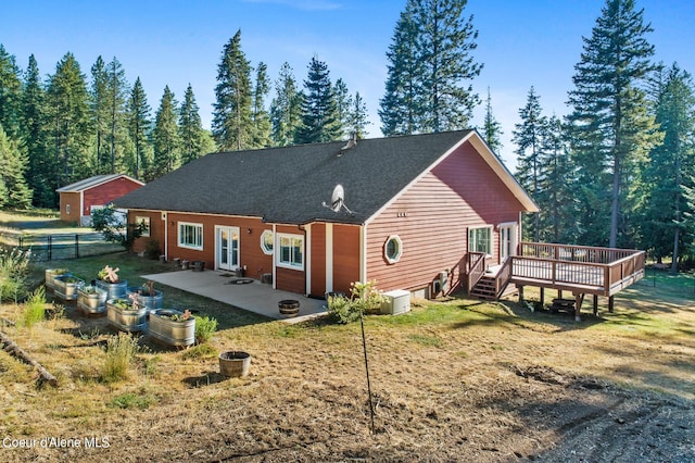 rear view of property featuring french doors, a wooden deck, a lawn, and a patio area