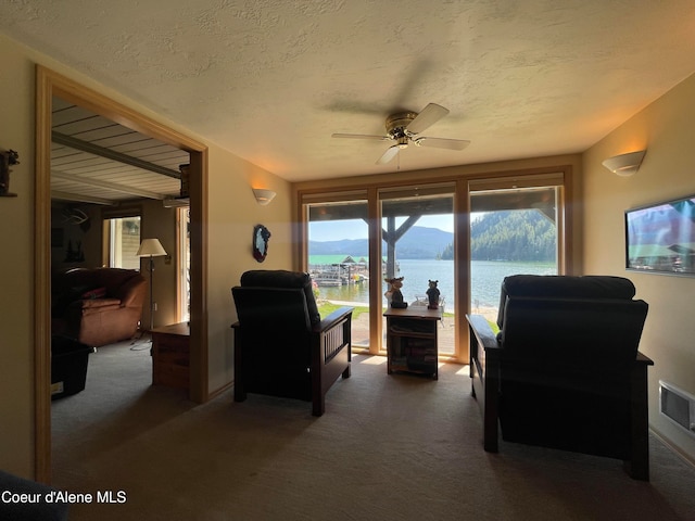 sitting room featuring a water view, dark colored carpet, a textured ceiling, and ceiling fan