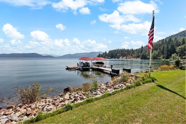 dock area with boat lift, a lawn, and a water and mountain view