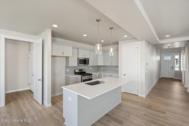 kitchen with sink, appliances with stainless steel finishes, a kitchen island with sink, white cabinets, and decorative light fixtures