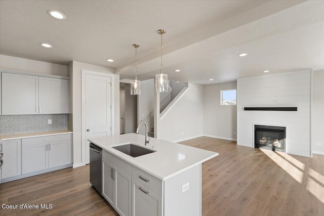 kitchen with sink, light hardwood / wood-style flooring, dishwasher, hanging light fixtures, and an island with sink