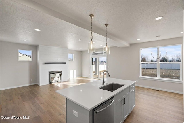 kitchen featuring sink, light hardwood / wood-style floors, dishwasher, pendant lighting, and a kitchen island with sink