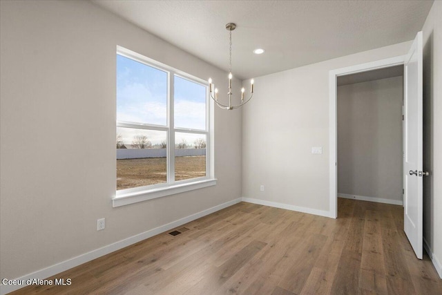 unfurnished dining area featuring an inviting chandelier and hardwood / wood-style flooring