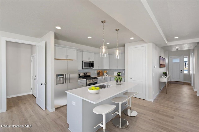 kitchen featuring sink, a breakfast bar, appliances with stainless steel finishes, an island with sink, and decorative light fixtures