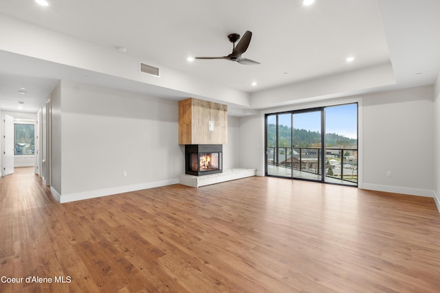 unfurnished living room featuring light wood finished floors, baseboards, a ceiling fan, a multi sided fireplace, and recessed lighting