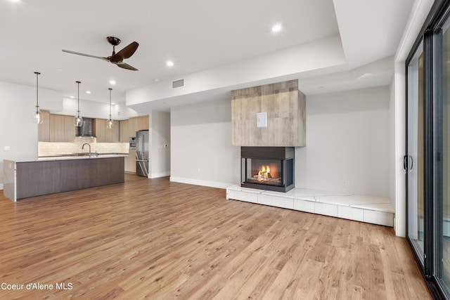 unfurnished living room with a tile fireplace, visible vents, ceiling fan, and light wood finished floors