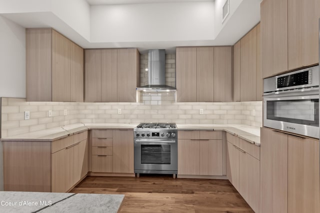 kitchen with wall chimney range hood, appliances with stainless steel finishes, backsplash, and light brown cabinetry