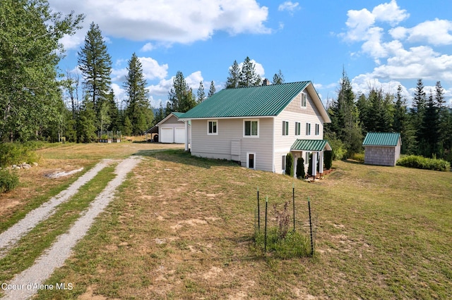 view of side of home featuring driveway, a lawn, metal roof, a storage unit, and an outdoor structure