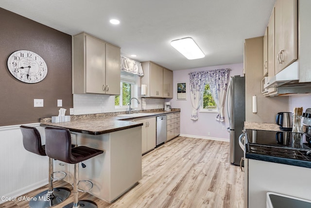 kitchen featuring dark countertops, appliances with stainless steel finishes, cream cabinetry, under cabinet range hood, and a sink