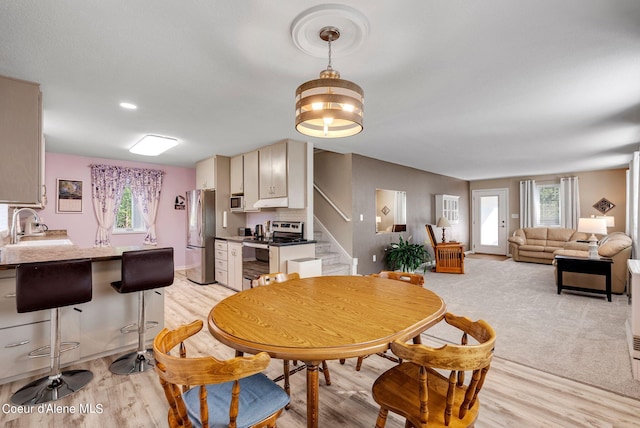 dining area featuring baseboards, light colored carpet, stairway, and light wood finished floors