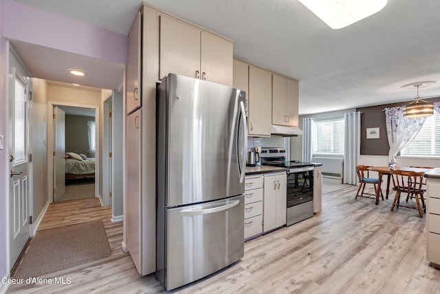 kitchen with light wood finished floors, dark countertops, cream cabinets, stainless steel appliances, and under cabinet range hood