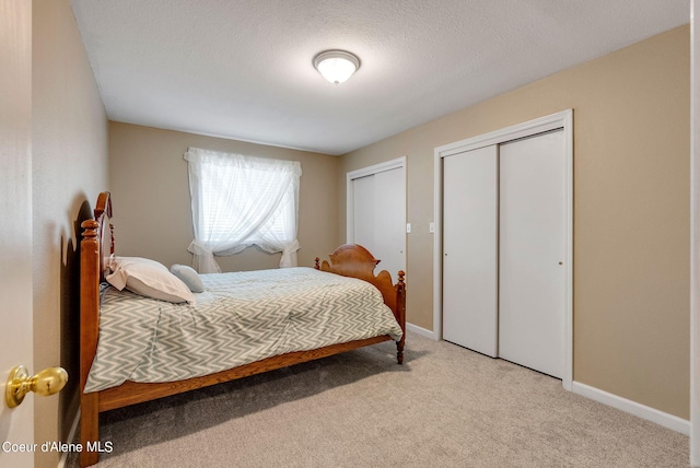 bedroom featuring baseboards, a textured ceiling, two closets, and light colored carpet