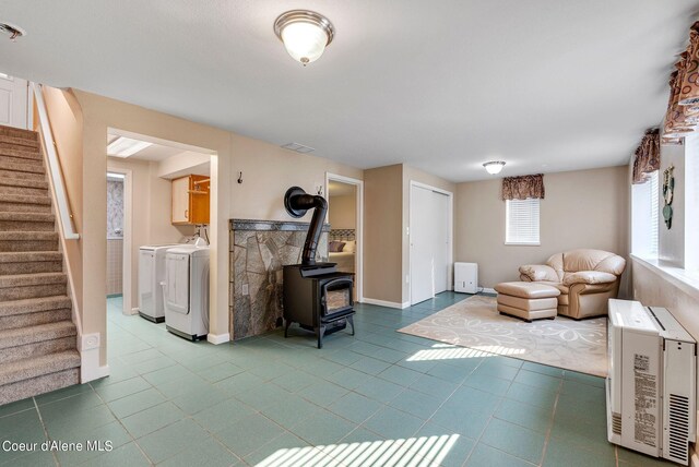 living room with tile patterned flooring, stairway, heating unit, washing machine and clothes dryer, and a wood stove