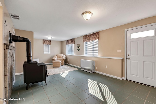 foyer entrance with heating unit, visible vents, a wood stove, baseboards, and tile patterned floors