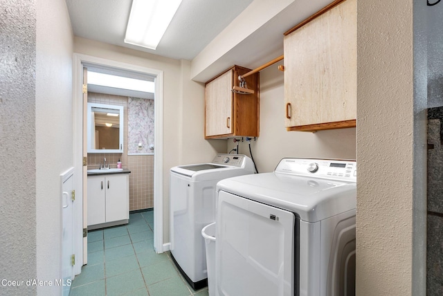 clothes washing area with cabinet space, washing machine and clothes dryer, a sink, tile walls, and light tile patterned flooring