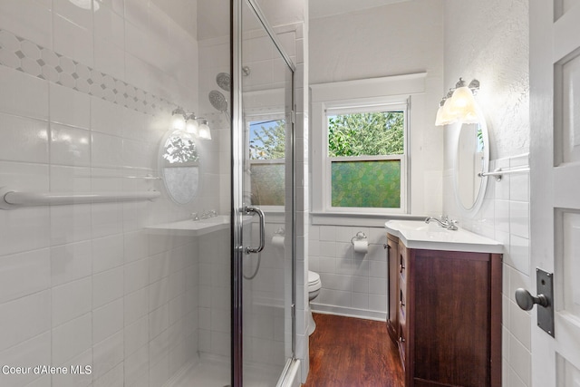 bathroom with a shower with shower door, toilet, vanity, tile walls, and hardwood / wood-style floors