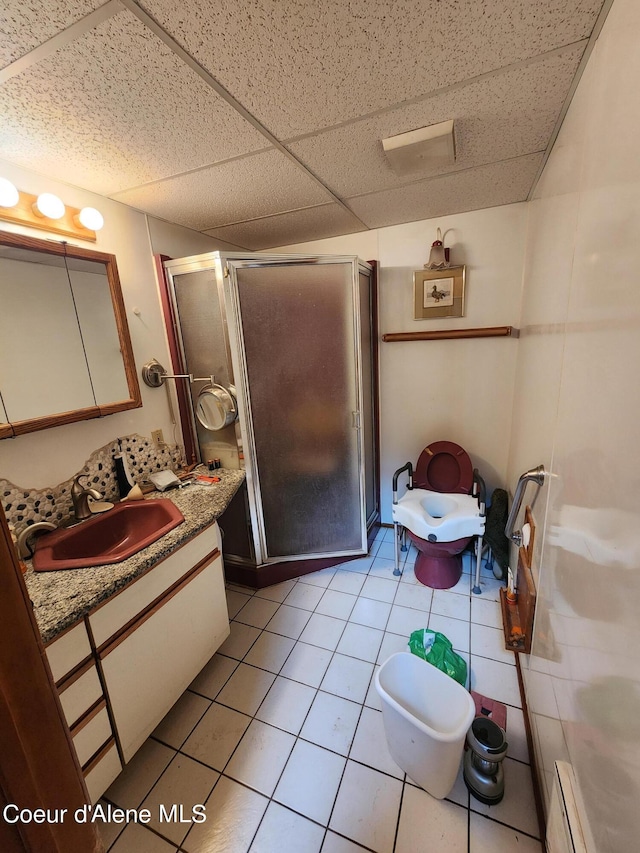 bathroom with a drop ceiling, vanity, a shower with door, baseboard heating, and tile patterned flooring