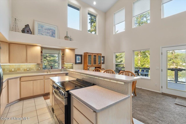 kitchen featuring tasteful backsplash, light brown cabinetry, a center island, and stainless steel electric range oven