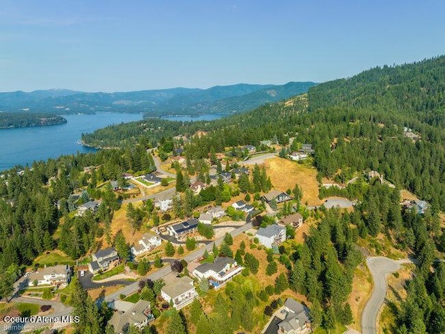 birds eye view of property featuring a water and mountain view, a wooded view, and a residential view