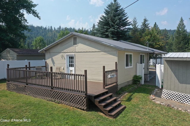 back of property featuring a wooden deck, a lawn, metal roof, and fence