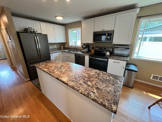 kitchen featuring visible vents, light wood finished floors, a sink, black appliances, and white cabinetry